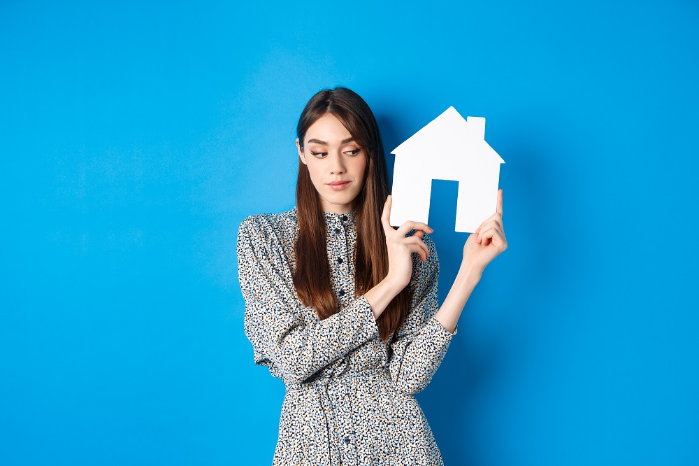 Mujer sostiene una casa de cart&oacute;n